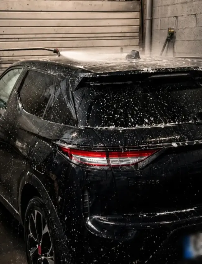 SUV noir couvert de mousse sous le jet haute pression, en station